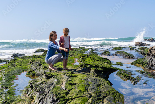 Mother pointing to daughter at rocky beach on sunny day photo