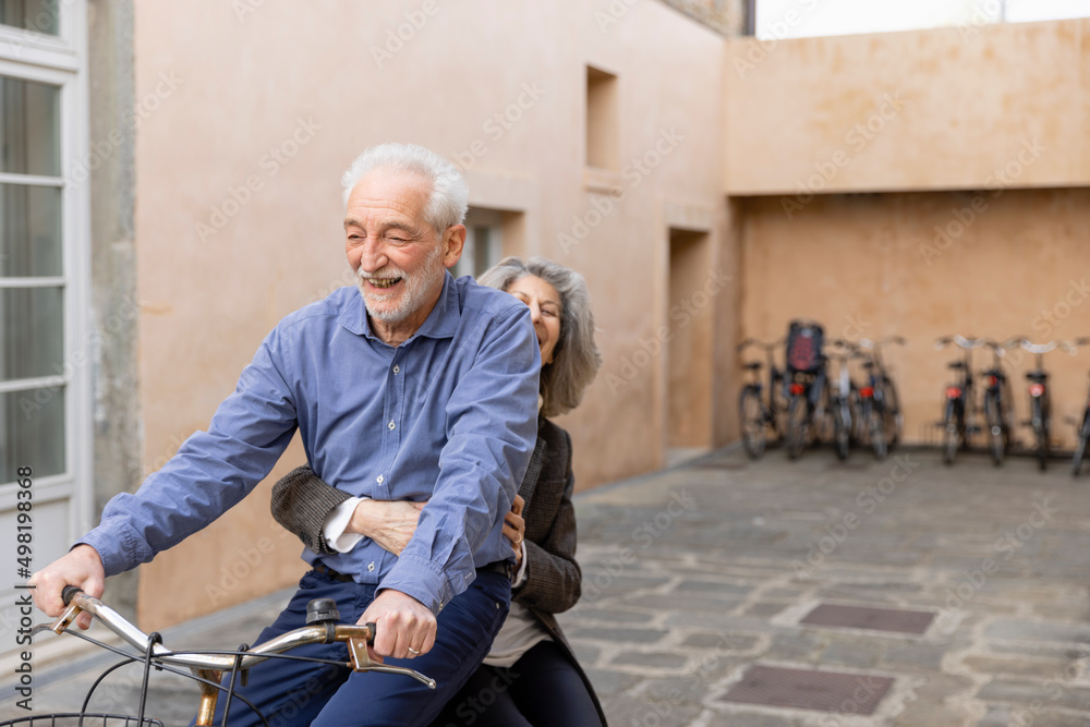 Senior woman sitting with man riding bicycle outside building Senior woman sitting with man riding bicycle outside building
