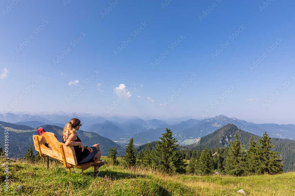 Germany, Bavaria, Female hiker relaxing on bench at summit of Fockenstein mountain Germany, Bavaria, Female hiker relaxing on bench at summit of Fockenstein mountain