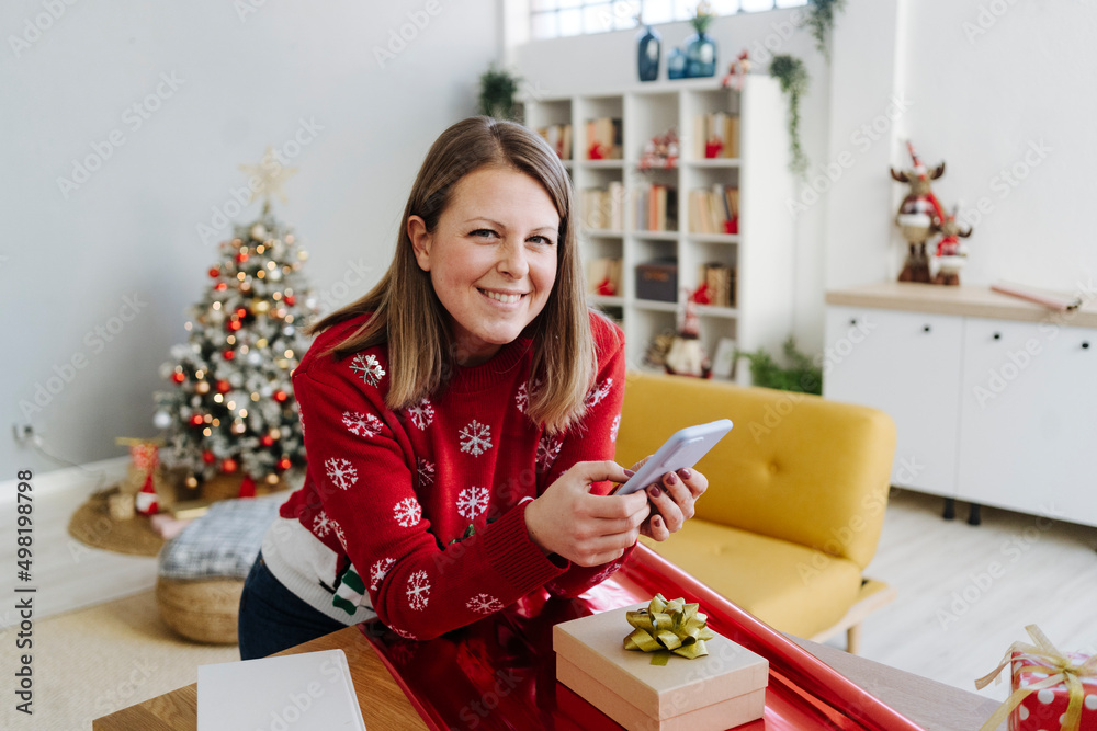 Smiling blond woman with mobile phone leaning on table at home Smiling blond woman with mobile phone leaning on table at home