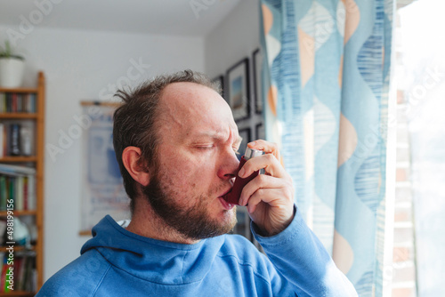 Man with eyes closed using asthma inhaler at home photo