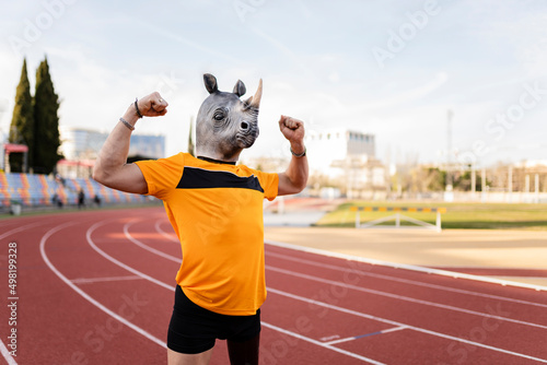 Man in rhinoceros face mask flexing biceps on running track photo