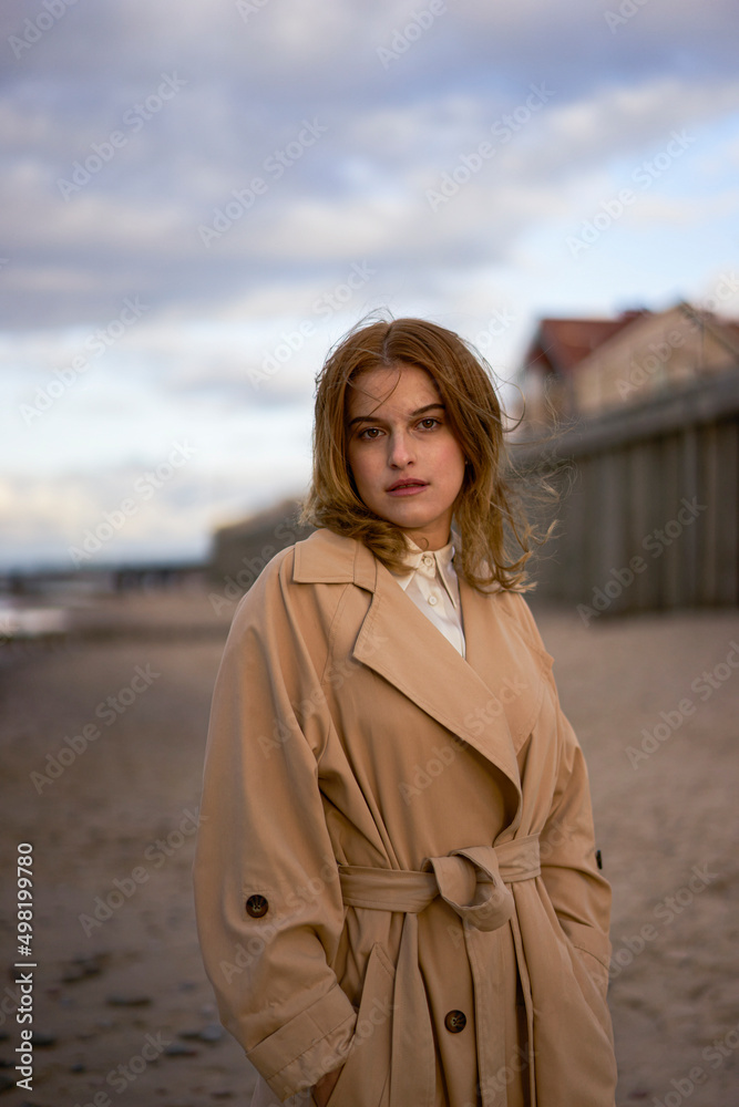 Beautiful woman with hands in pockets standing on beach at sunset Beautiful woman with hands in pockets standing on beach at sunset