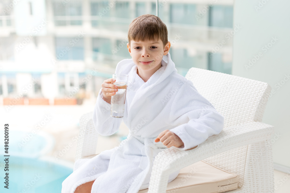 A European child holds a glass of clean water in the fresh air. A boy in a white coat. A European child holds a glass of clean water in the fresh air. A boy in a white coat.