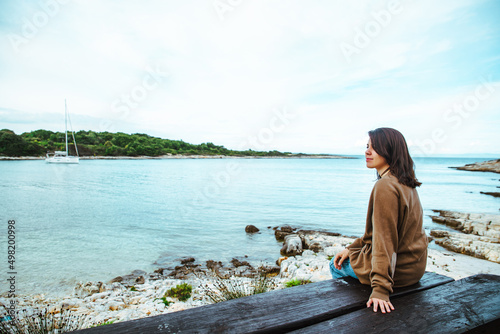 woman sitting on bench looking on yacht in bay