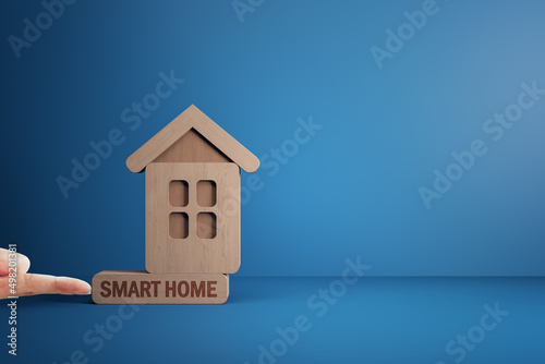 Finger pushing abstract wooden house on blue mortgage backdrop with mock up place. Smart home, oan, bank and money concept. photo