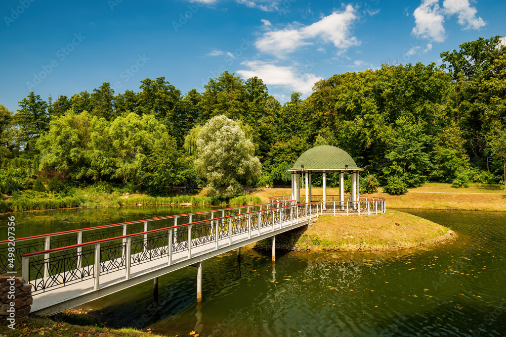 Small island in the center of park pond with round gazebo and pedestrian bridge. Feofaniya public park, Kyiv, Ukraine
