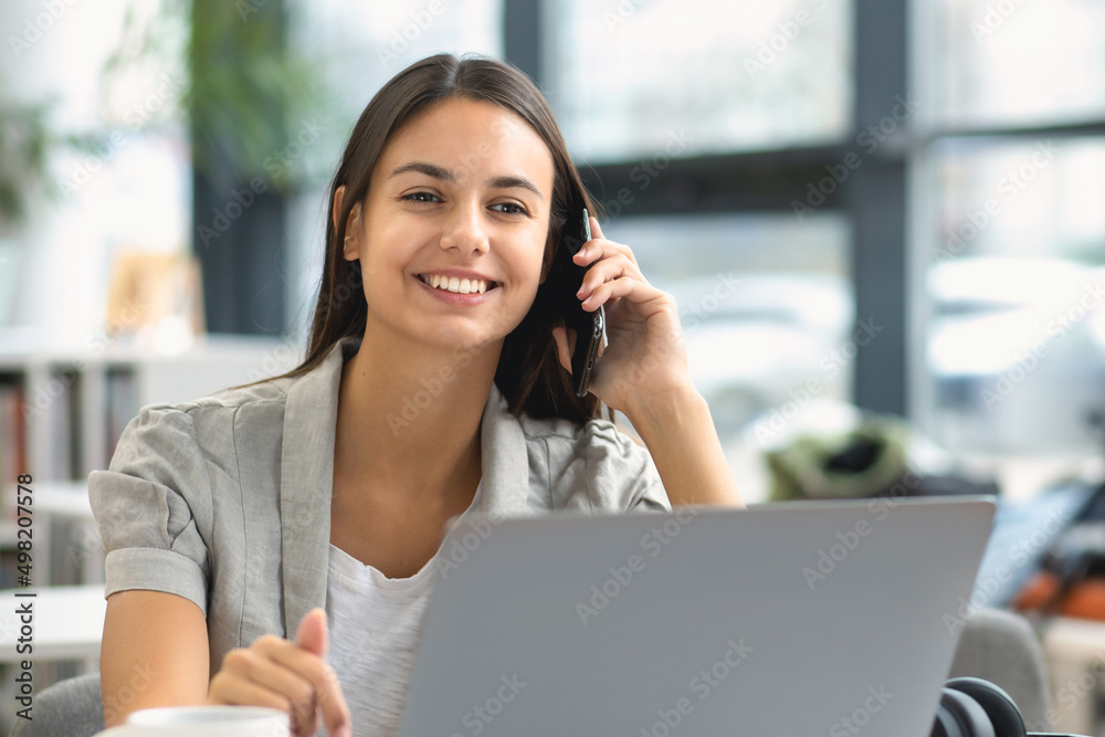 Beautiful caucasian young woman working, talking on the phone while sitting at the workplace in the office Beautiful caucasian young woman working, talking on the phone while sitting at the workplace in the office