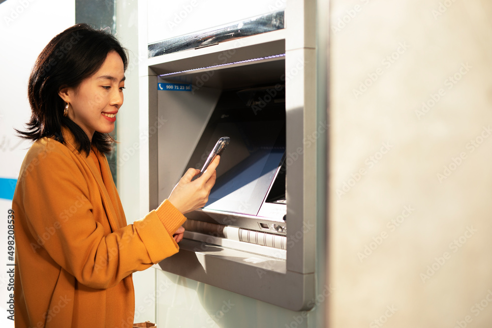 Happy smiling young woman withdrawing money from credit card. Young woman typing pin code on keypad of ATM machine. Happy smiling young woman withdrawing money from credit card. Young woman typing pin code on keypad of ATM machine.