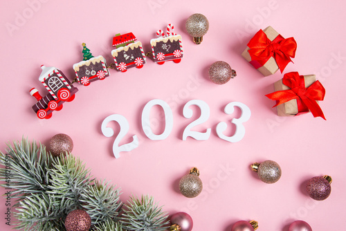 White numbers in the shape of 2023 and New Year's baubles on a pink background. Flat lay with place for text.