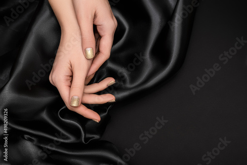 Female hands with golden nail design. Glitter gold nail polish manicure. Female model hands on black fabric background