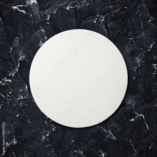 Blank white beer coaster on black plaster background. Responsive design mockup. Top view. Flat lay.