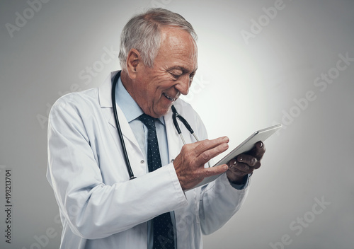 This is great news for my patient. Shot of an elderly doctor using a digital tablet in a studio against a grey background.