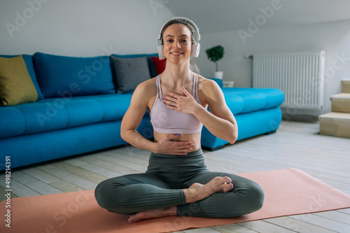 Woman in a lotus position practicing yoga at home and using headphones