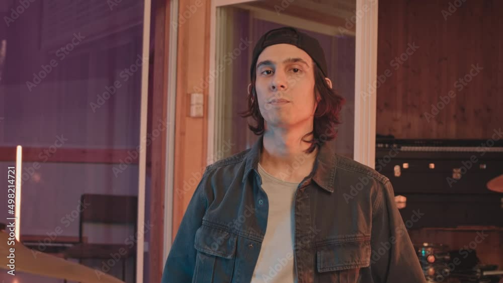 Medium slowmo portrait of young Caucasian male drummer at music studio throwing wooden stick and hitting on drum plate making sound then looking at camera