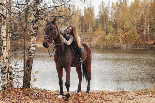 Cute young woman on horse in autumn forest by lake © Alex Vog