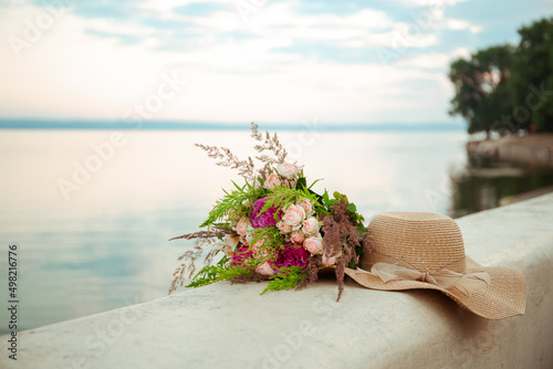 Tableau sur toile Straw hat with flower bouquet lay on the embankment on the sky and sea nature background