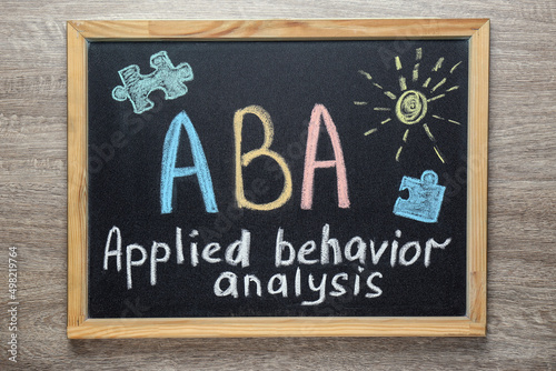 Small blackboard with text ABA Applied behavior analysis and drawings on wooden table, top view photo