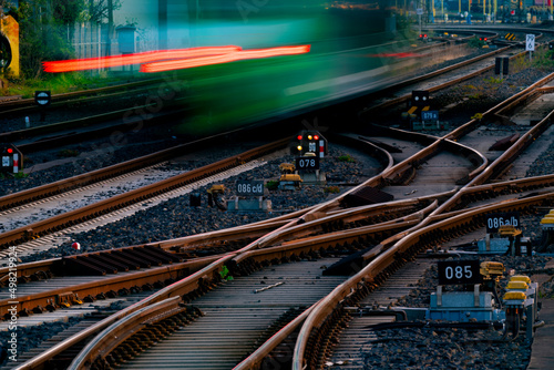 Railway tracks at main station of Hagen Westphalia Germany with switches and blurred leaving train in motion. Railway infrastructure and technology background at morning twilight. 