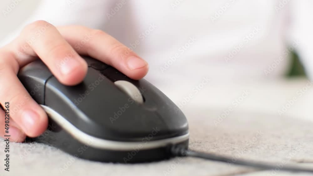 The childs hand moves the computer mouse to the sides while playing a video game or working on a laptop. The boy presses buttons with his fingers, does homework or online education concept. Close-up. The childs hand moves the computer mouse to the sides while playing a video game or working on a laptop. The boy presses buttons with his fingers, does homework or online education concept. Close-up.