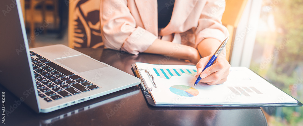 Woman analyzing data graph the stock situation.She uses a pen and a laptop computer.