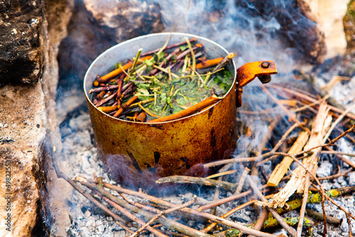 Survival in wild nature. Campfire background. Pan with cherry tea sticks over fire. Cooking tea drink at fire in wild.