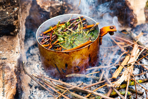 Survival in wild nature. Campfire background. Pan with cherry tea sticks over fire. Cooking tea drink at fire in wild.