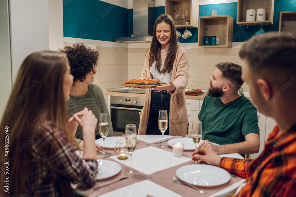 Group of friends enjoying dinner while sitting at the kitchen table together Group of friends enjoying dinner while sitting at the kitchen table together