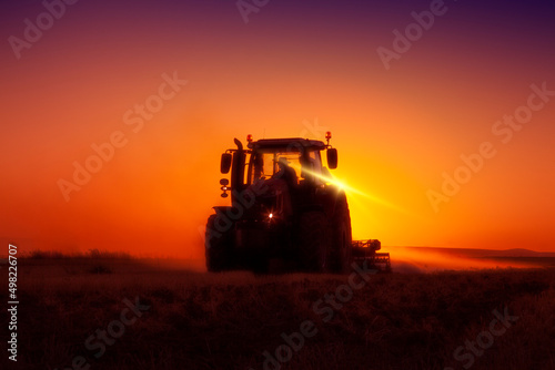 Farmer ploughs a field with tractor in sunset. The tractor is backlit by the setting sun. 