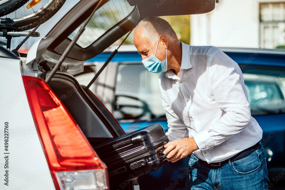 A taxi or Uber driver in mask puts the luggage into the trunk of the car A taxi or Uber driver in mask puts the luggage into the trunk of the car