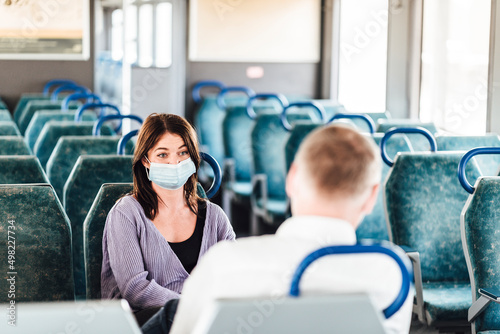 A couple of friends wearing mask and talking while traveling by train
