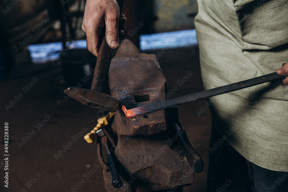 The blacksmith manually forging the red-hot metal on the anvil in smithy. The blacksmith manually forging the red-hot metal on the anvil in smithy.