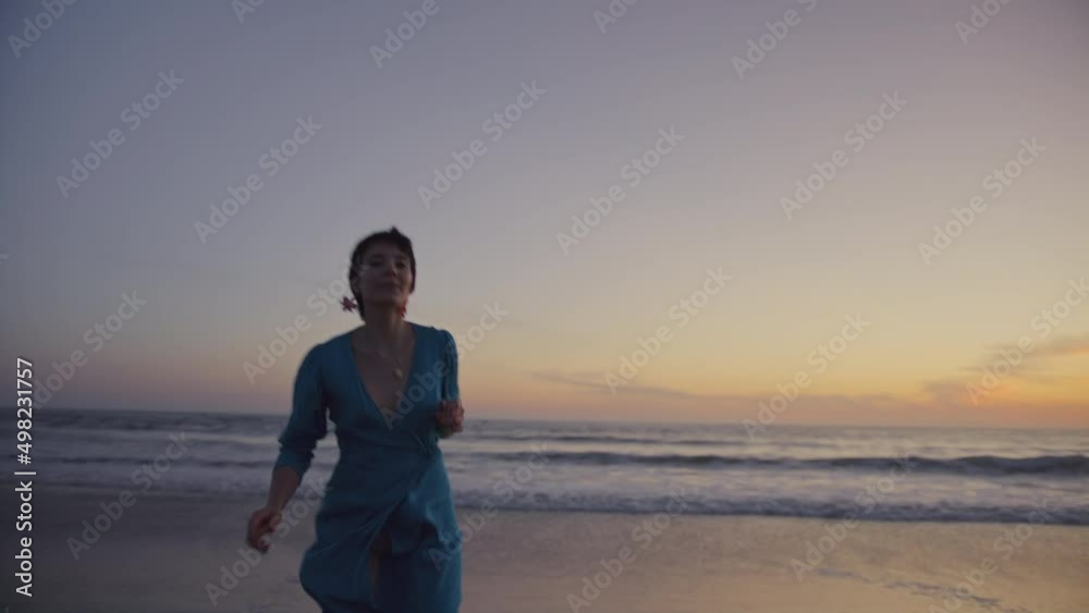 Young beautiful lady running near water at warm splendid sandy shore wearing blue romantic flattering trendy dress, dark boots. Cheerful girl flirting, dancing near sea, ocean during travel, vacation Young beautiful lady running near water at warm splendid sandy shore wearing blue romantic flattering trendy dress, dark boots. Cheerful girl flirting, dancing near sea, ocean during travel, vacation