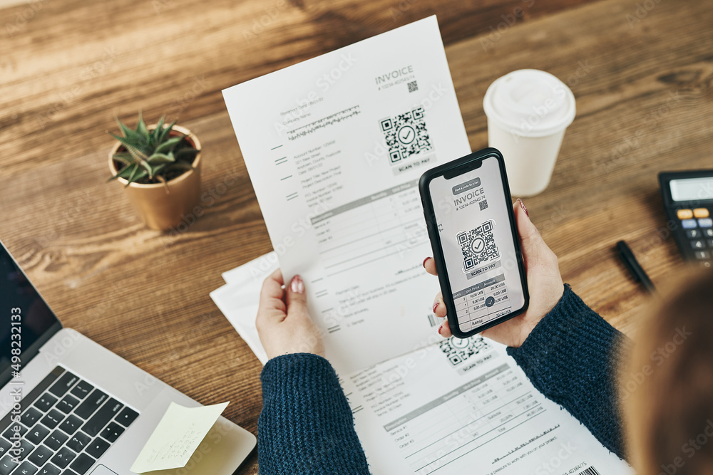 Woman paying invoice scanning QR code from document using fast secure payment system and smartphone QR scanner. Business woman paying bills using express payment technology. Paying expenses online - obrazy, fototapety, plakaty 