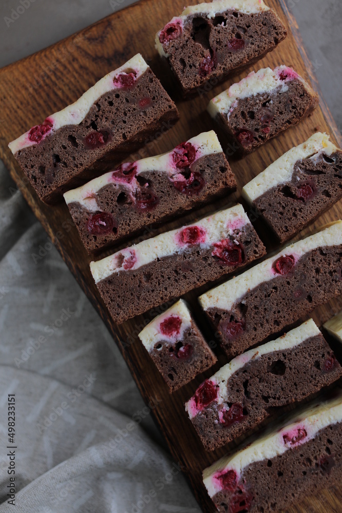 Chocolate brownie with cherries and cheese layer. Many pieces of chocolate dessert with berries on a wooden board Chocolate brownie with cherries and cheese layer. Many pieces of chocolate dessert with berries on a wooden board