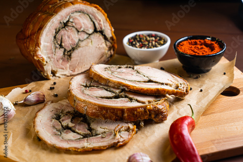 Porchetta on wooden board with chili pepper, garlic and paprika