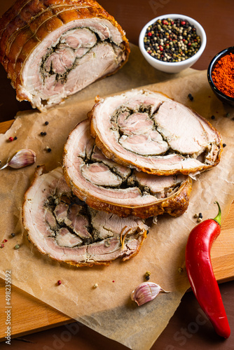 Porchetta on wooden board with chili pepper, garlic and paprika