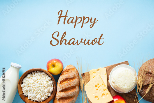 Happy Shavuot concept. Dairy products, bread, fruits, wheat on blue background. Jewish holiday eating. photo