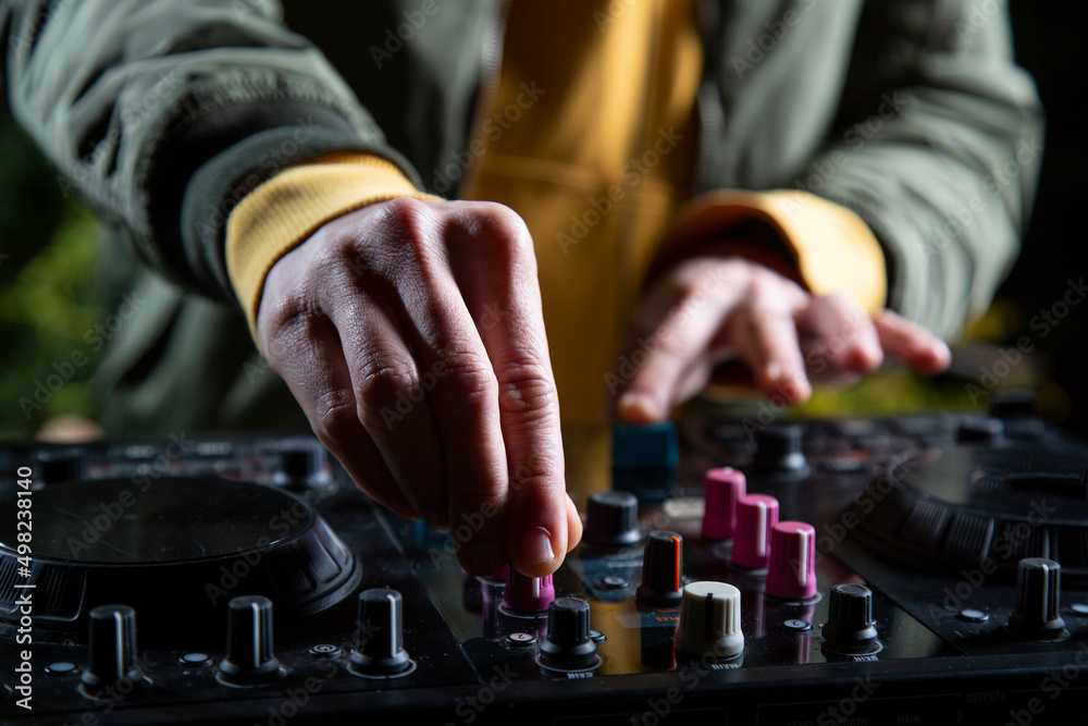 manos DJ chico pincha musica con una mesa de mezclas en una fiesta en bosque vestido con una chaqueta verde, una sudadera con capucha y una gorra, rave party manos DJ chico pincha musica con una mesa de mezclas en una fiesta en bosque vestido con una chaqueta verde, una sudadera con capucha y una gorra, rave party
