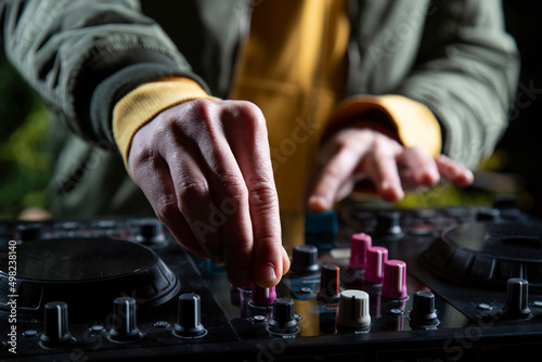 manos DJ chico pincha musica con una mesa de mezclas en una fiesta en bosque vestido con una chaqueta verde, una sudadera con capucha y una gorra, rave party
