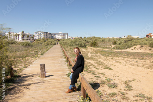 A red-haired Caucasian woman on a wooden walkway, on the beach of Isla Cristina, Huelva, Spain.