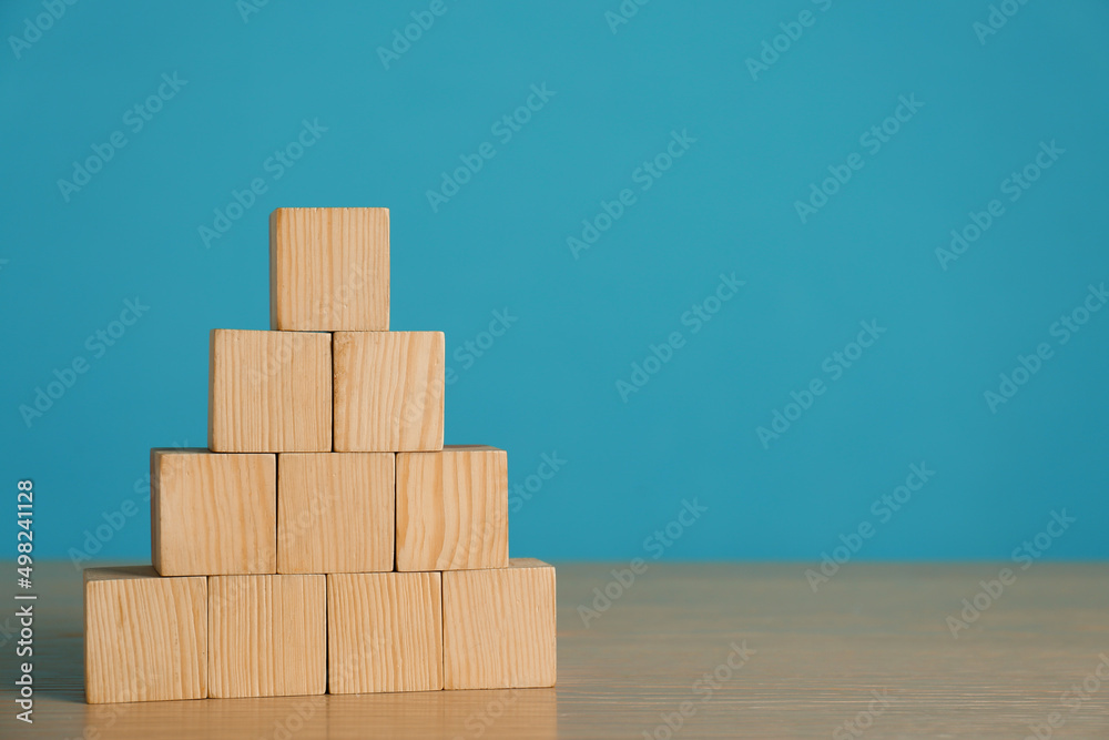 Pyramid of blank cubes on wooden table against light blue background. Space for text Pyramid of blank cubes on wooden table against light blue background. Space for text