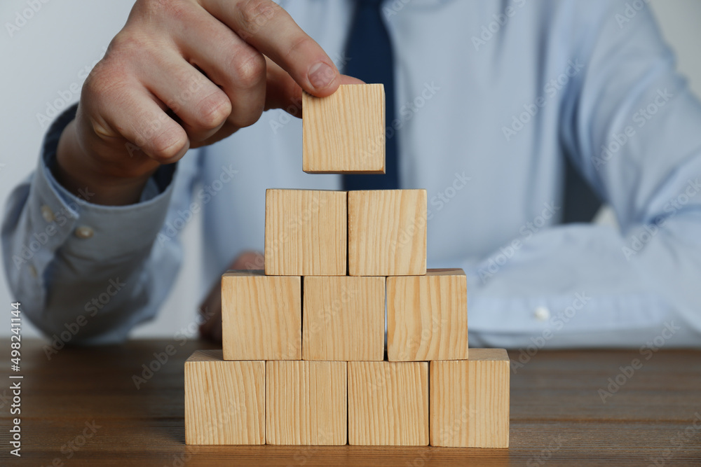 Businessman building pyramid of blank cubes on wooden table, closeup. Space for text Businessman building pyramid of blank cubes on wooden table, closeup. Space for text