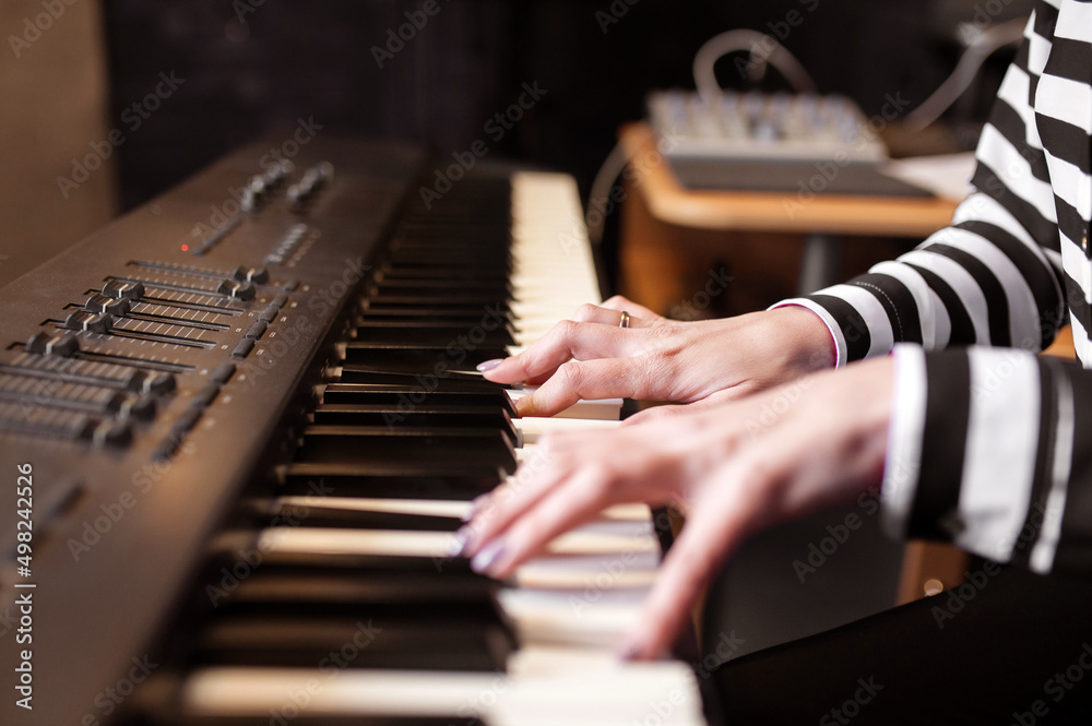 Obraz premium Woman playing piano record music on synthesizer using notes and laptop. Female hands musician pianist improves skills playing piano. Online Music education hobby vocals singing. Long web banner.