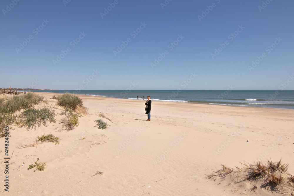 A Caucasian woman with red hair on the beach of Isla Cristina, Huelva, Spain. A blue sky and fine sand. Concept of the best beaches.