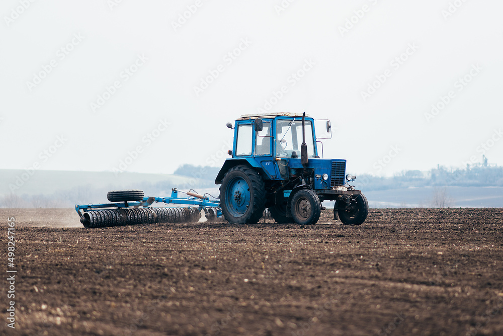 Obraz premium The tractor processes the field in spring. combine harvester in work on sowing wheat