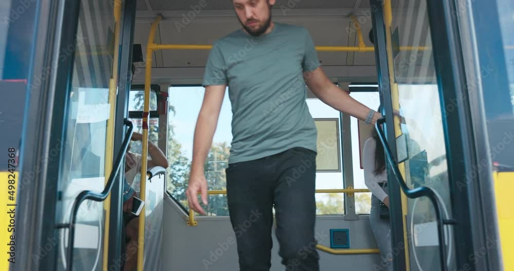 The doors of a public transportation vehicle open after coming to a stop. A man gets off the bus followed by a student and a woman of African-American descent, people from the street get on the bus The doors of a public transportation vehicle open after coming to a stop. A man gets off the bus followed by a student and a woman of African-American descent, people from the street get on the bus