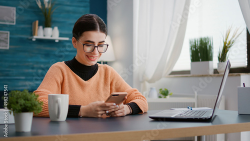 College student browsing internet on smartphone to do reseacrh for online school assignment. Woman using mobile phone to type and take notes for class lesson information and knowledge. photo