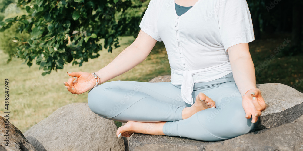 Close-up of caucasian yogi woman sitting in lotus position on stone in nature. Yoga and meditation outdoors. Selective focus Close-up of caucasian yogi woman sitting in lotus position on stone in nature. Yoga and meditation outdoors. Selective focus