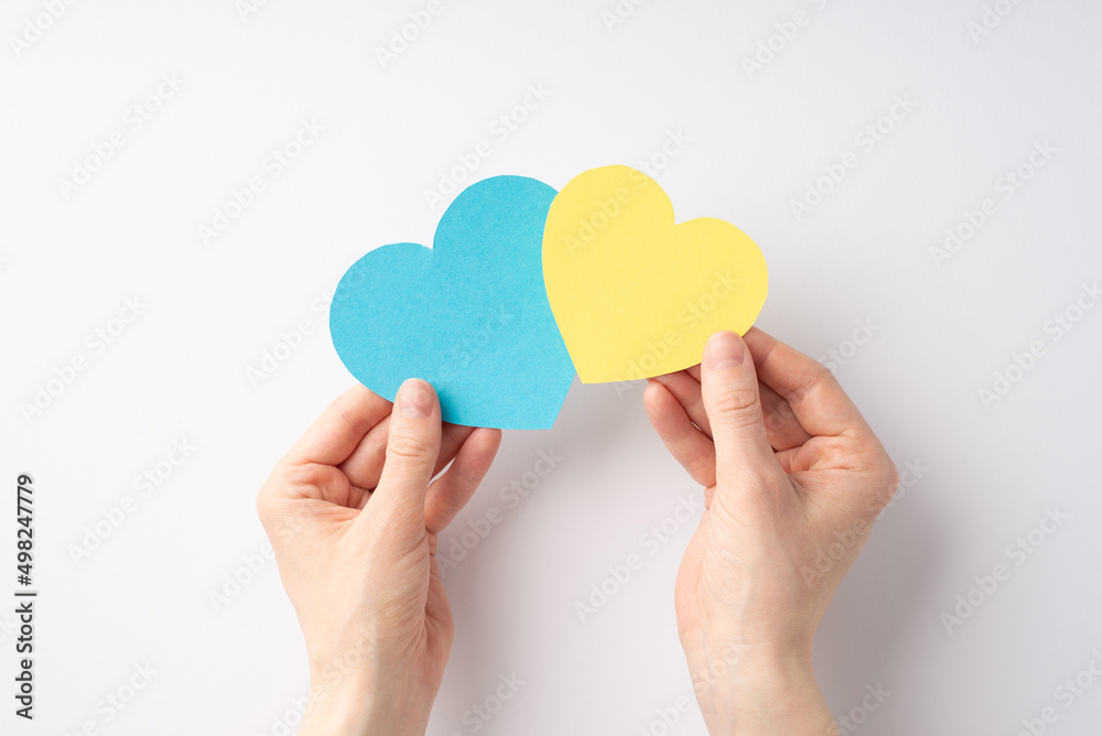 Obraz premium Stop the war in Ukraine concept. First person top view photo of girl's hands holding two yellow and blue hearts on white background